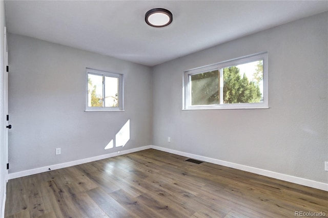 empty room featuring dark wood-style floors, visible vents, and baseboards