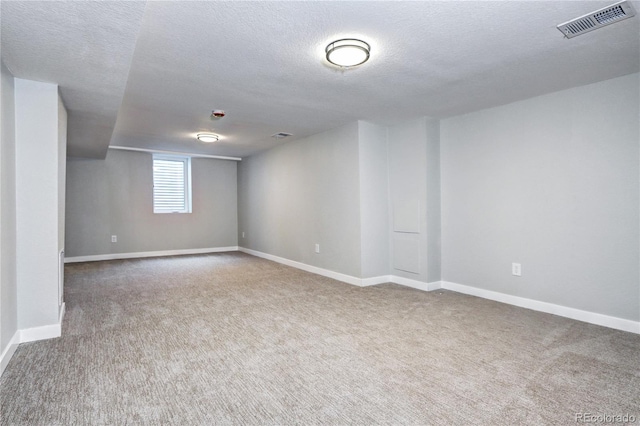 basement featuring a textured ceiling, carpet, visible vents, and baseboards