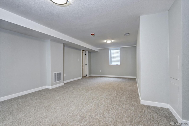 basement featuring a textured ceiling, carpet flooring, visible vents, and baseboards