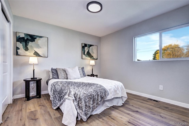 bedroom featuring a closet, wood finished floors, visible vents, and baseboards