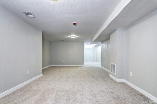 finished below grade area featuring light colored carpet, visible vents, and baseboards