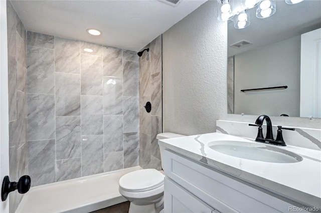 full bath featuring a stall shower, visible vents, a textured wall, toilet, and vanity