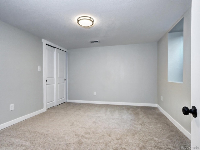 carpeted empty room featuring visible vents, a textured ceiling, and baseboards