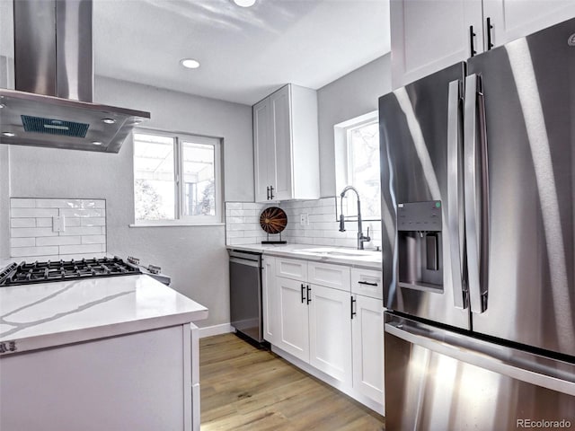 kitchen with a sink, appliances with stainless steel finishes, decorative backsplash, light wood finished floors, and island exhaust hood