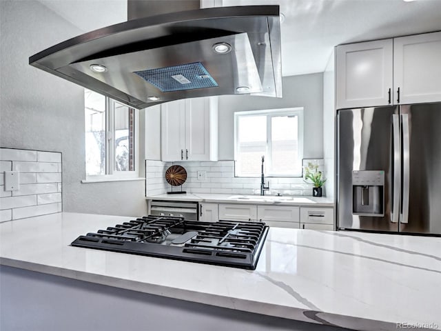 kitchen with stainless steel refrigerator with ice dispenser, tasteful backsplash, a sink, stovetop, and exhaust hood