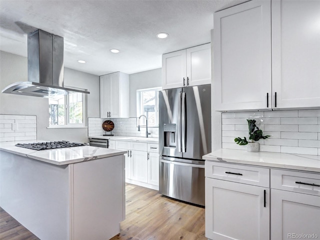 kitchen with gas cooktop, island range hood, white cabinetry, light wood finished floors, and stainless steel fridge