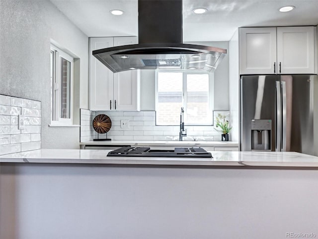 kitchen featuring light countertops, stainless steel refrigerator with ice dispenser, decorative backsplash, and island range hood