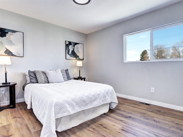 bedroom with baseboards, visible vents, and wood finished floors