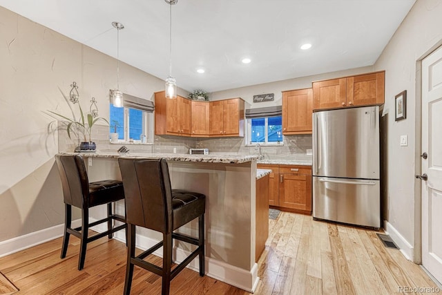 kitchen with freestanding refrigerator, a breakfast bar area, light wood finished floors, brown cabinets, and tasteful backsplash