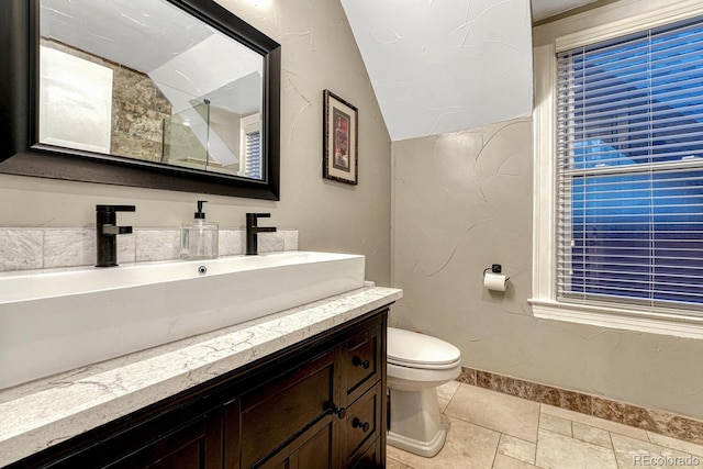 bathroom with vanity, toilet, baseboards, and stone tile flooring