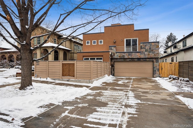 view of front of house with stucco siding, fence, driveway, a garage, and stone siding