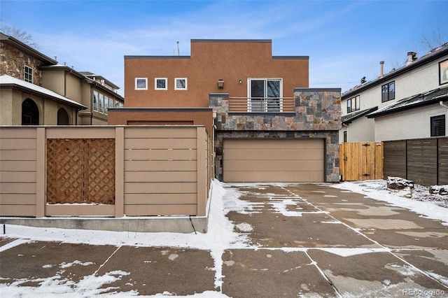 exterior space featuring stucco siding, an attached garage, fence, driveway, and stone siding