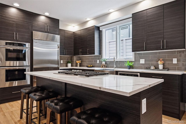 467 Harrison St, Denver, CO 80206 - kitchen featuring stainless steel appliances, a breakfast bar, backsplash, dark brown cabinetry, and modern cabinets
