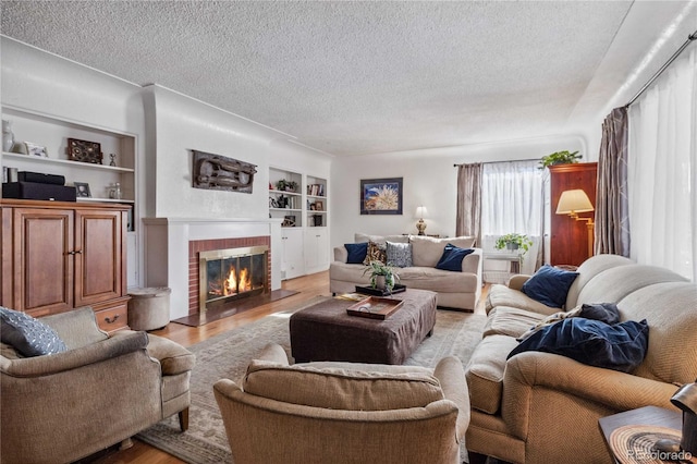 living room featuring built in shelves, a fireplace, light wood-type flooring, and a textured ceiling