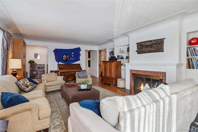 living room with wood-type flooring, a textured ceiling, a fireplace, and built in shelves