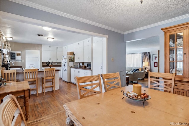 dining area with ornamental molding, a textured ceiling, and light hardwood / wood-style flooring