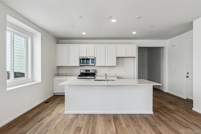 kitchen featuring white cabinetry, appliances with stainless steel finishes, a center island with sink, and light wood-type flooring