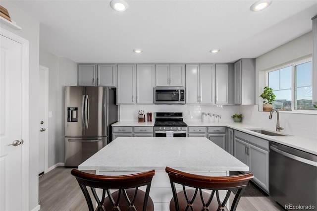 kitchen with stainless steel appliances, decorative backsplash, sink, light wood-type flooring, and gray cabinetry