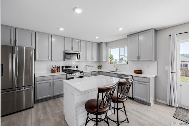 kitchen featuring appliances with stainless steel finishes, a center island, a kitchen bar, light hardwood / wood-style floors, and sink