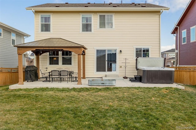 rear view of house featuring a gazebo, a hot tub, a lawn, and a patio