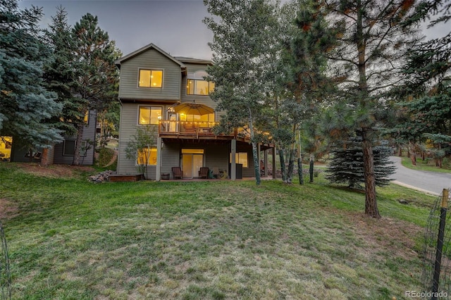 back house at dusk featuring a lawn and a balcony