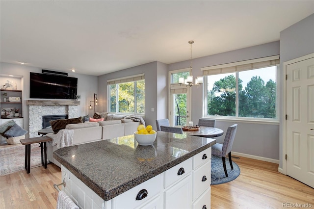 kitchen with white cabinets, hanging light fixtures, light wood-type flooring, a fireplace, and a notable chandelier