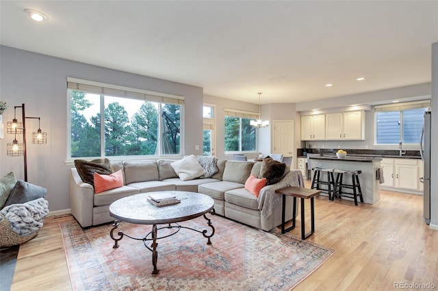 living room with a notable chandelier, sink, and light wood-type flooring