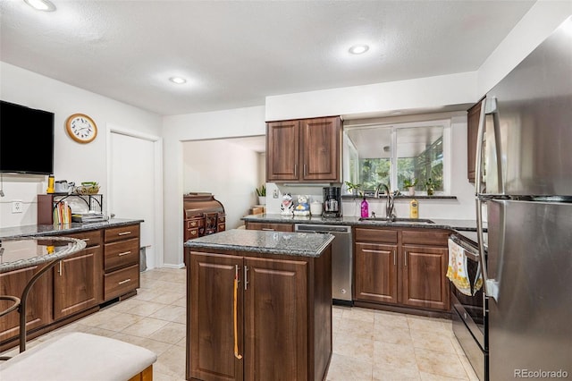 kitchen featuring dark stone countertops, a textured ceiling, a kitchen island, sink, and appliances with stainless steel finishes