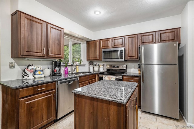 kitchen featuring dark stone countertops, a textured ceiling, a center island, sink, and appliances with stainless steel finishes