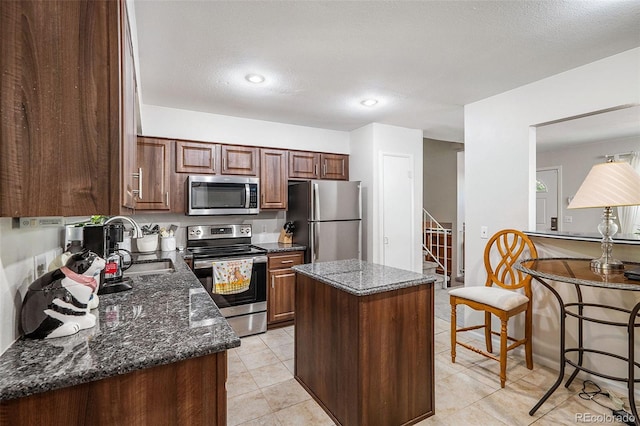 kitchen featuring a textured ceiling, appliances with stainless steel finishes, a center island, sink, and dark stone countertops