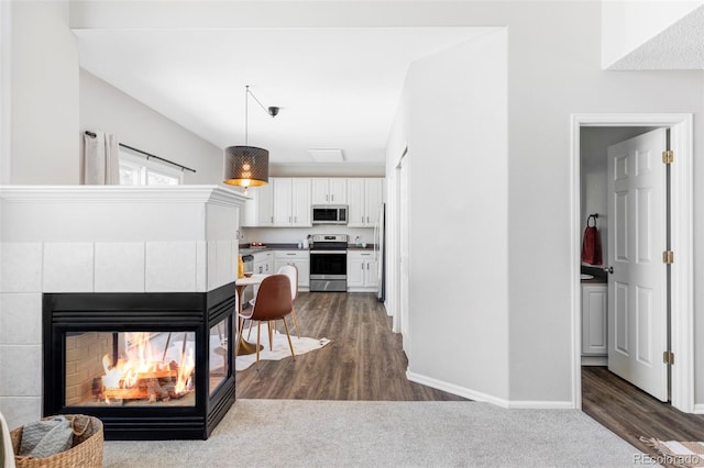 interior space featuring white cabinetry, decorative light fixtures, a multi sided fireplace, dark hardwood / wood-style floors, and stainless steel appliances