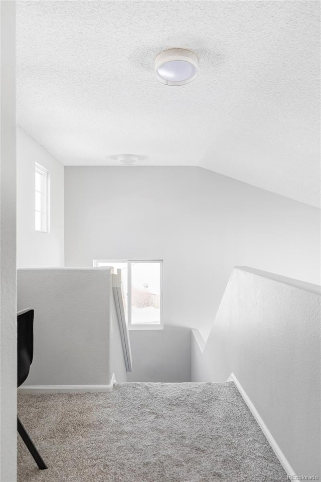 stairway with lofted ceiling, plenty of natural light, carpet, and a textured ceiling