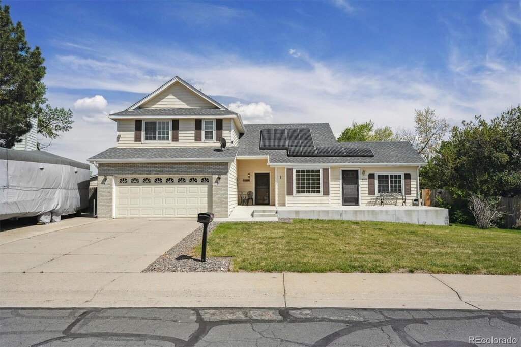 9908 Garfield Ct, Thornton, CO 80229 - traditional home featuring an attached garage, driveway, solar panels, a front lawn, and roof with shingles