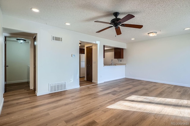 unfurnished living room with a sink, a textured ceiling, wood finished floors, and visible vents