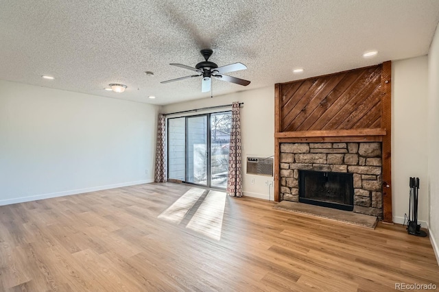 unfurnished living room with a stone fireplace, a wall mounted AC, light wood-type flooring, and baseboards