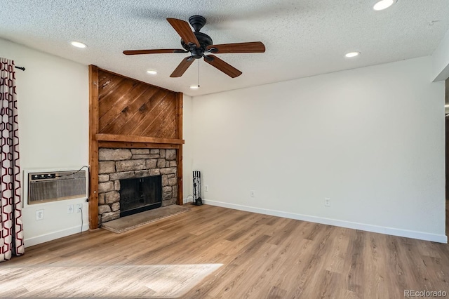 unfurnished living room with a textured ceiling, a stone fireplace, wood finished floors, baseboards, and a wall mounted air conditioner