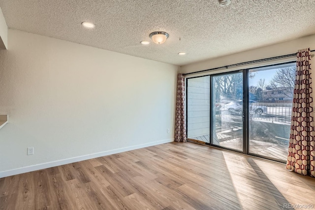 spare room featuring a textured ceiling, light wood finished floors, and baseboards