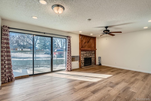 unfurnished living room with a textured ceiling, a stone fireplace, baseboards, and wood finished floors