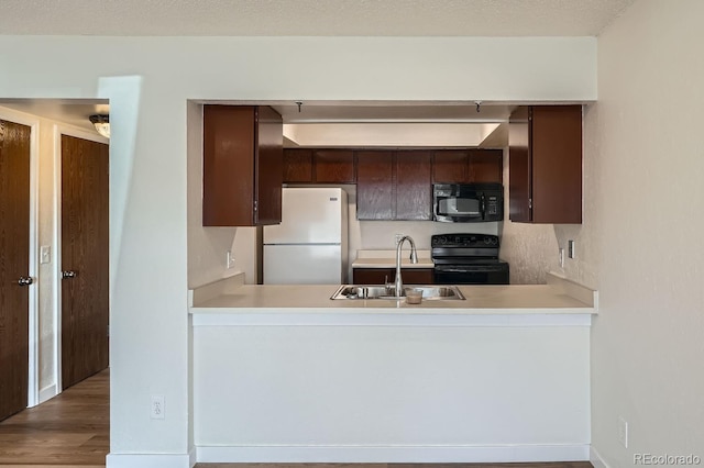 kitchen with dark brown cabinetry, a peninsula, a sink, light countertops, and black appliances