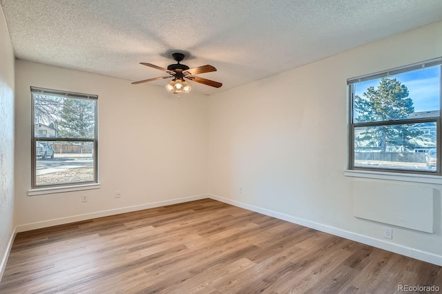 empty room with ceiling fan, light wood-style flooring, baseboards, and a textured ceiling