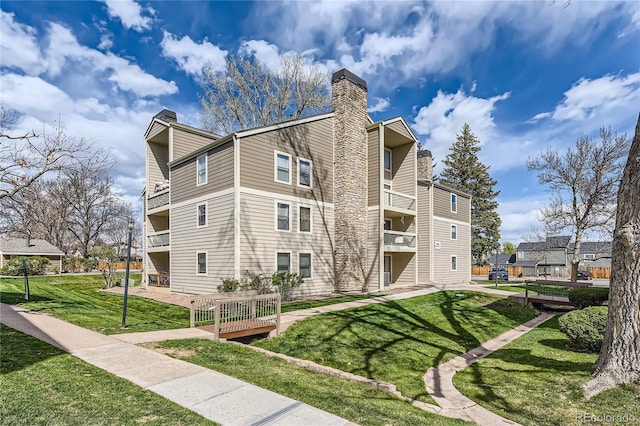 exterior space featuring a lawn, a chimney, and a balcony