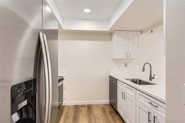 kitchen with a sink, stainless steel appliances, light wood-style flooring, white cabinets, and baseboards