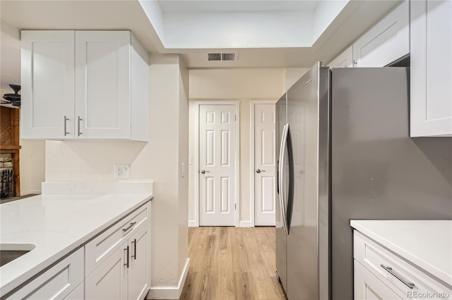 kitchen featuring light wood finished floors, white cabinetry, light stone countertops, visible vents, and freestanding refrigerator
