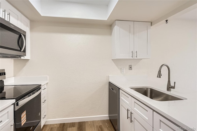 kitchen featuring stainless steel appliances, light countertops, wood finished floors, a sink, and baseboards
