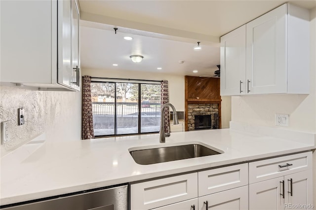 kitchen featuring stainless steel dishwasher, a ceiling fan, a sink, backsplash, and white cabinetry