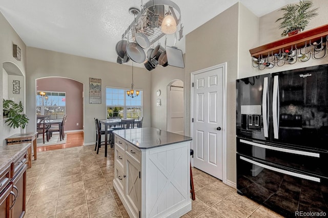 55610 E 40th Ave, Strasburg, CO 80136 - kitchen with black refrigerator with ice dispenser, arched walkways, a chandelier, and white cabinetry