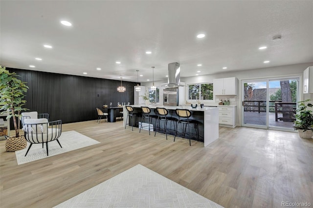 kitchen featuring a breakfast bar area, island exhaust hood, stainless steel fridge with ice dispenser, white cabinets, and recessed lighting