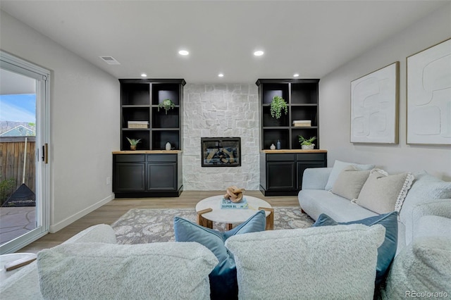 living area with a stone fireplace, light wood-style flooring, recessed lighting, baseboards, and visible vents