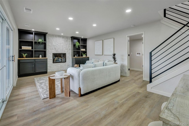 living room featuring stairs, baseboards, light wood-style flooring, and a fireplace