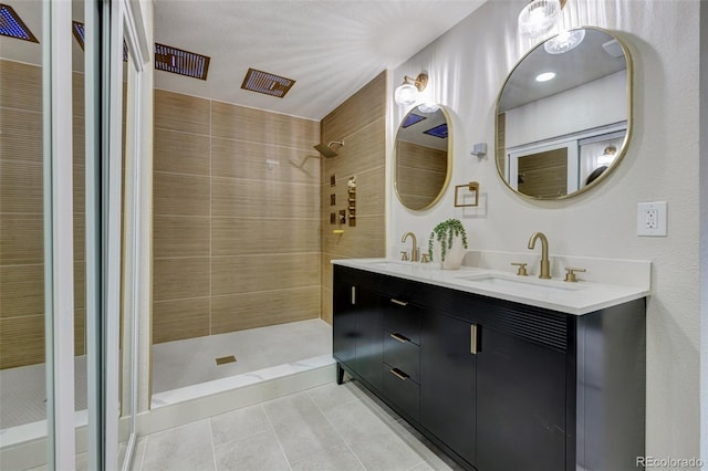 bathroom with double vanity, tile patterned floors, tiled shower, and a sink